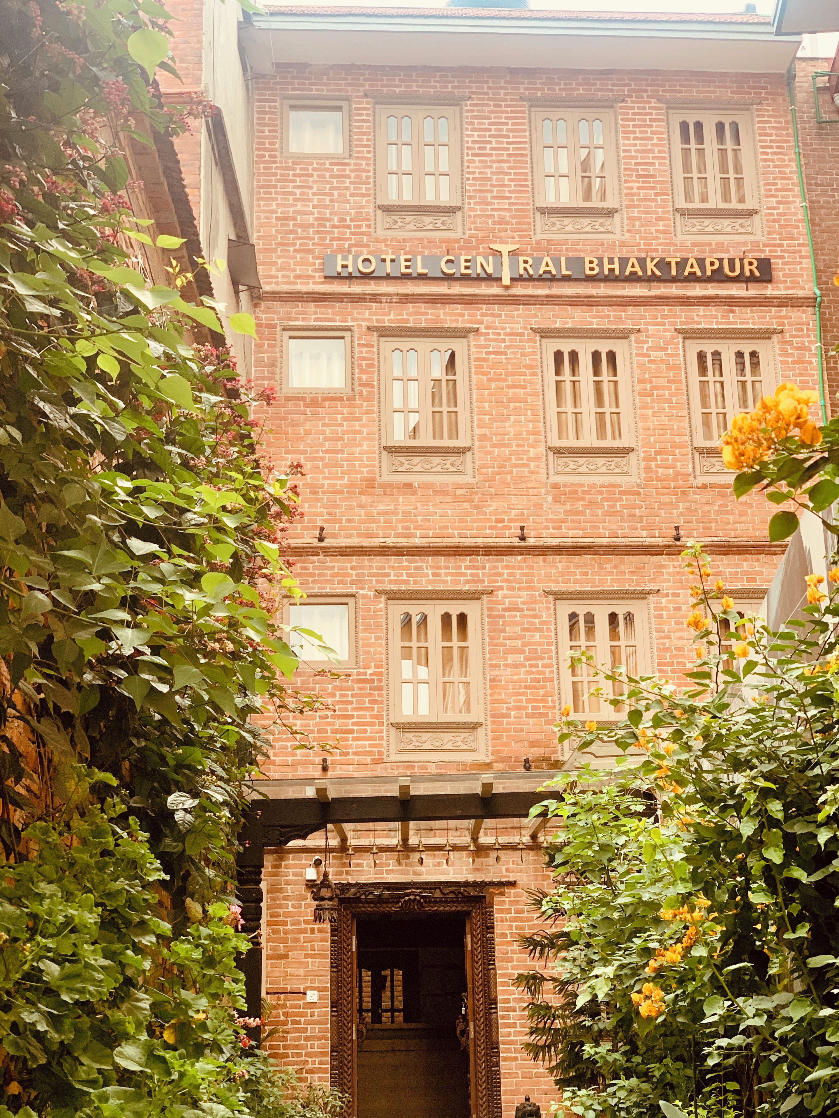 Un bâtiment en briques avec une enseigne indiquant « HÔTEL CENTRAL BHAKTAPUR » et une porte d’entrée.
