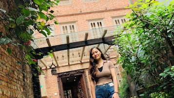 Una persona de pie en un patio con un edificio de ladrillo que dice 'CENTRAL BHAKTAPUR' al fondo.