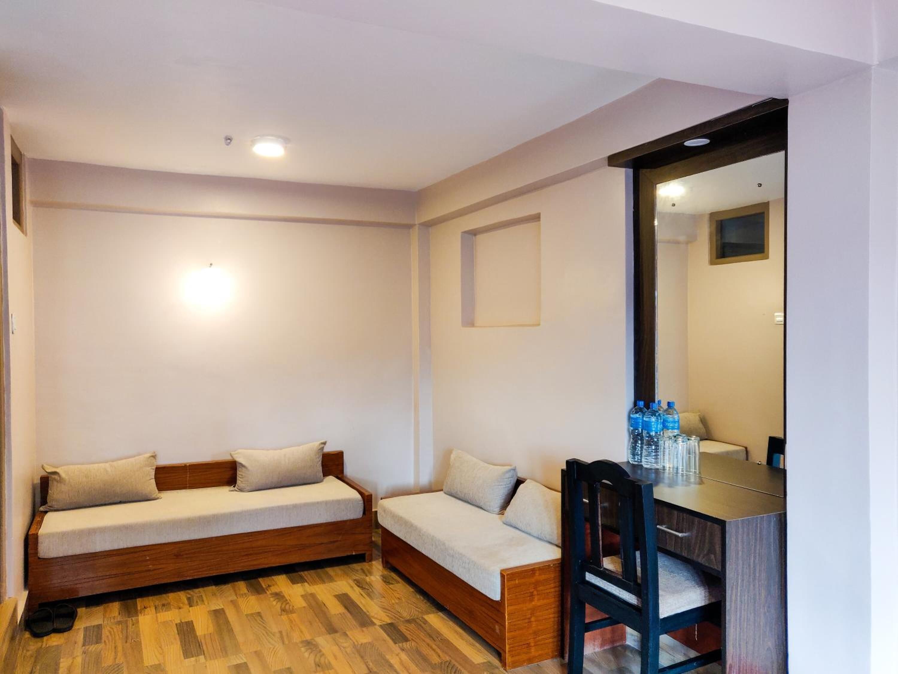 A small, cozy room with a wooden floor, a wooden sofa, a small table with a chair, and a mirror on the wall.