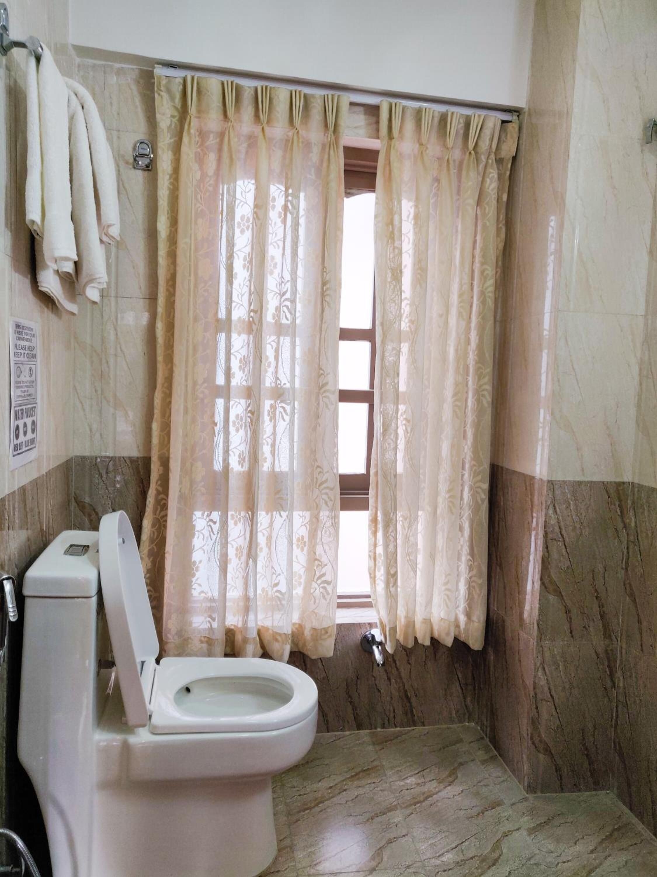 A bathroom with a toilet, a shower curtain, and a marble wall.