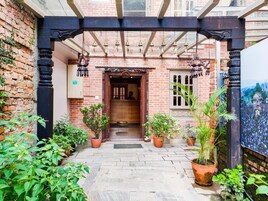 Un patio con muro de ladrillo, plantas en macetas y una puerta de madera que da a un espacio interior.