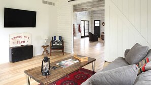 Un salon avec un plancher en bois, un canapé gris, une table basse surmontée d’une lanterne, un fauteuil et un tapis rouge.