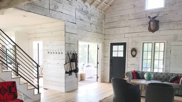 Un salon spacieux doté de parquets en bois, d’un escalier, d’un canapé gris et d’une tête de cerf fixée au mur.