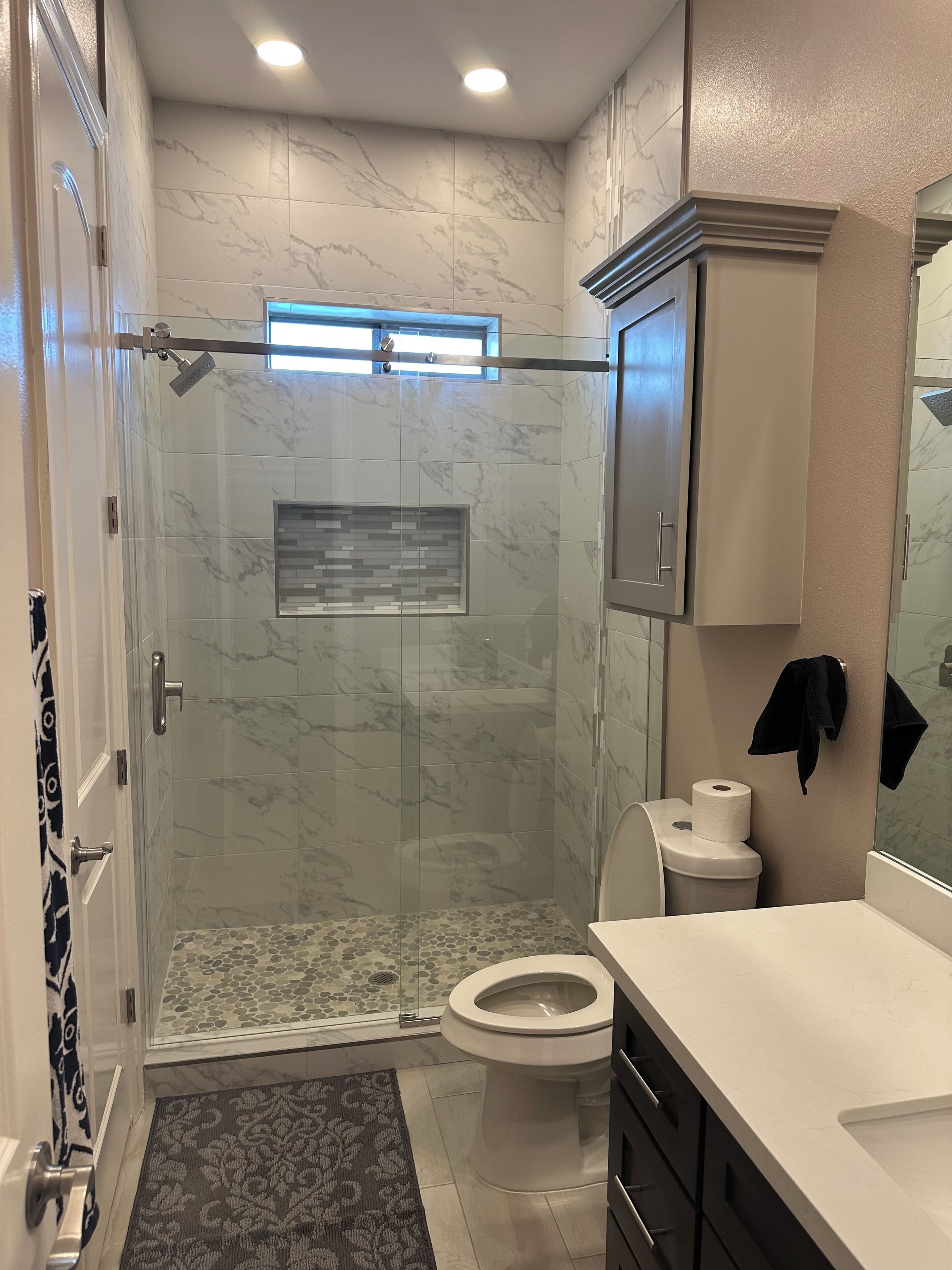 Une salle de bain moderne avec une douche à parois de verre, des toilettes et un meuble-lavabo avec des placards.