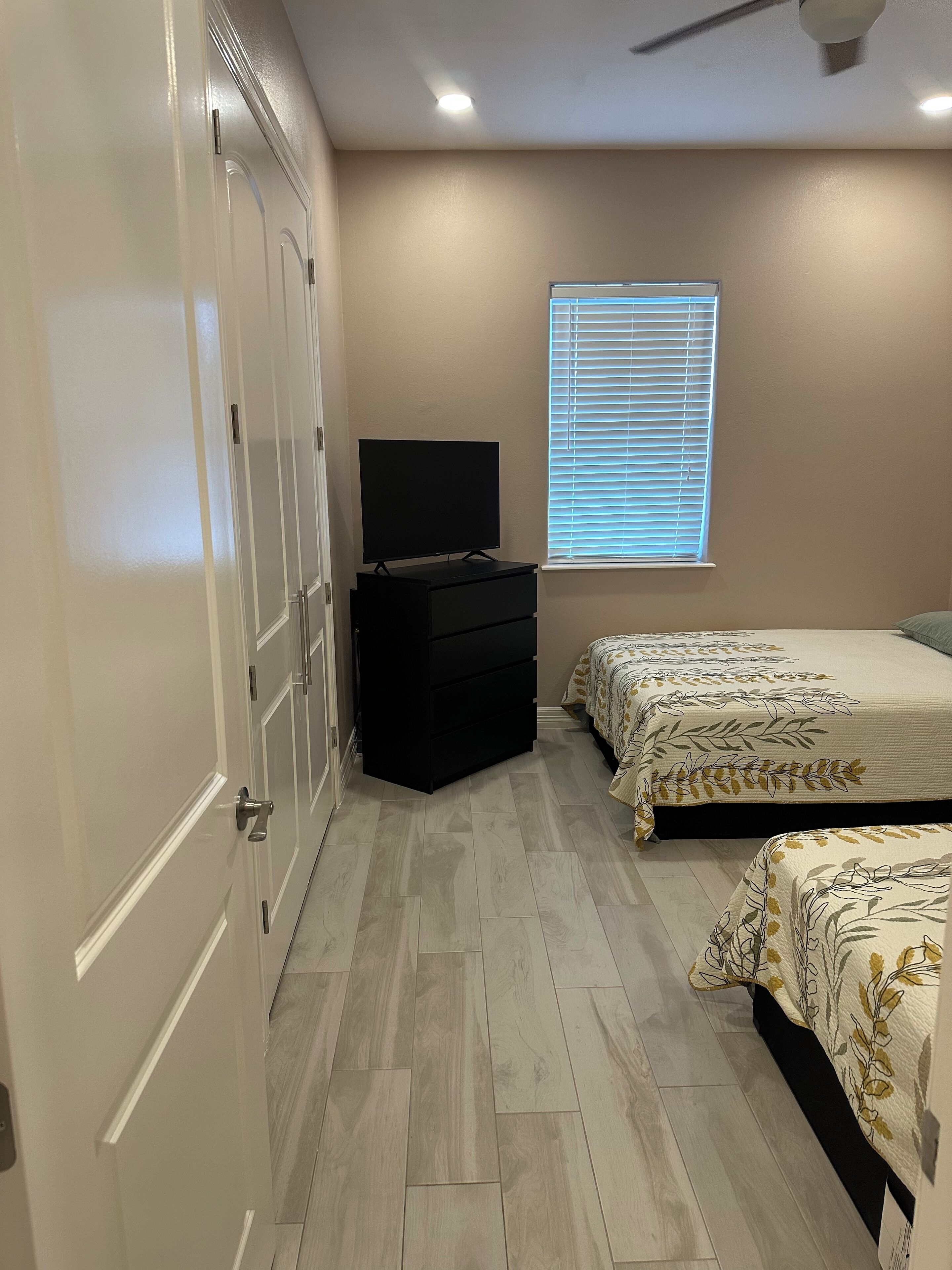A bedroom with a bed, a dresser, a TV, and a window with blinds.