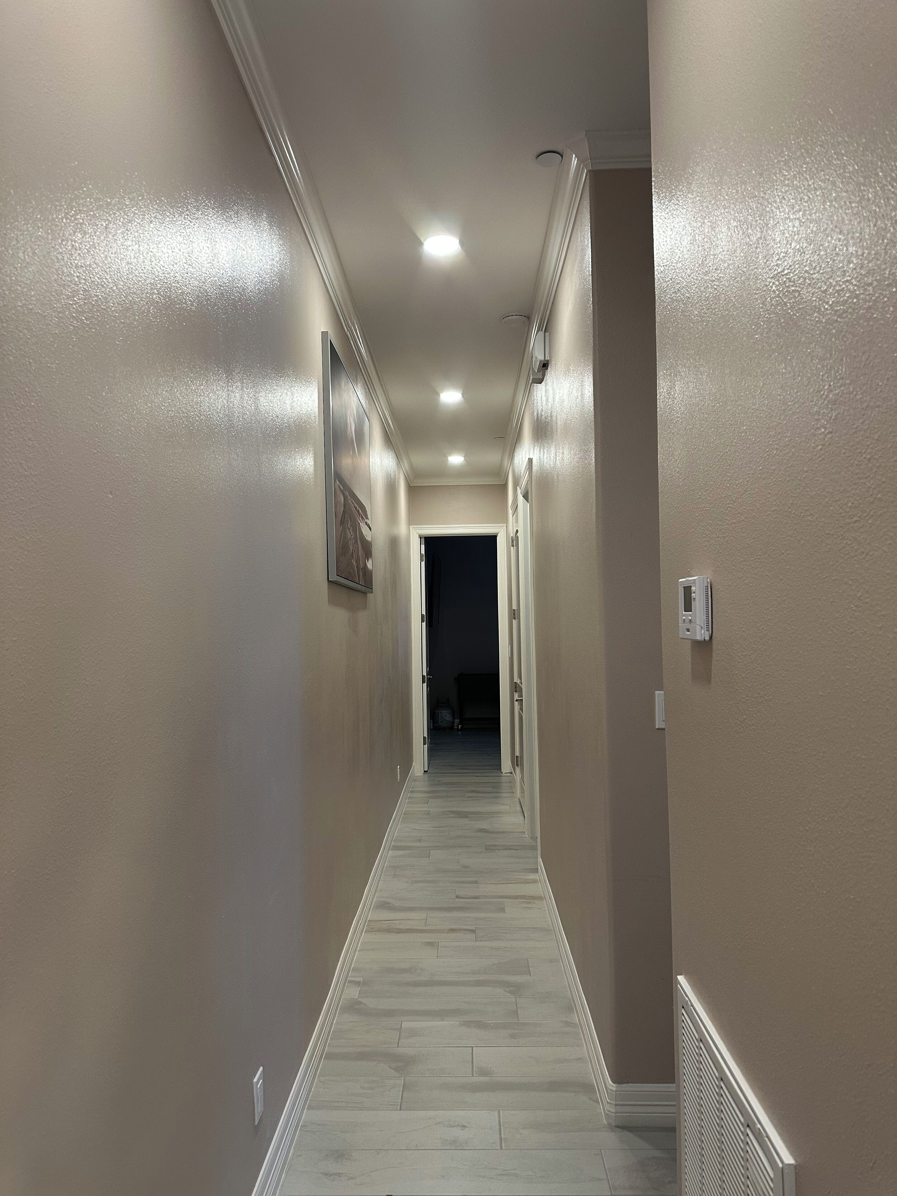 Un pasillo con paredes color beige, piso de madera e iluminación empotrada en el techo.