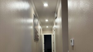 Um corredor com paredes bege, piso de madeira e teto com iluminação embutida.