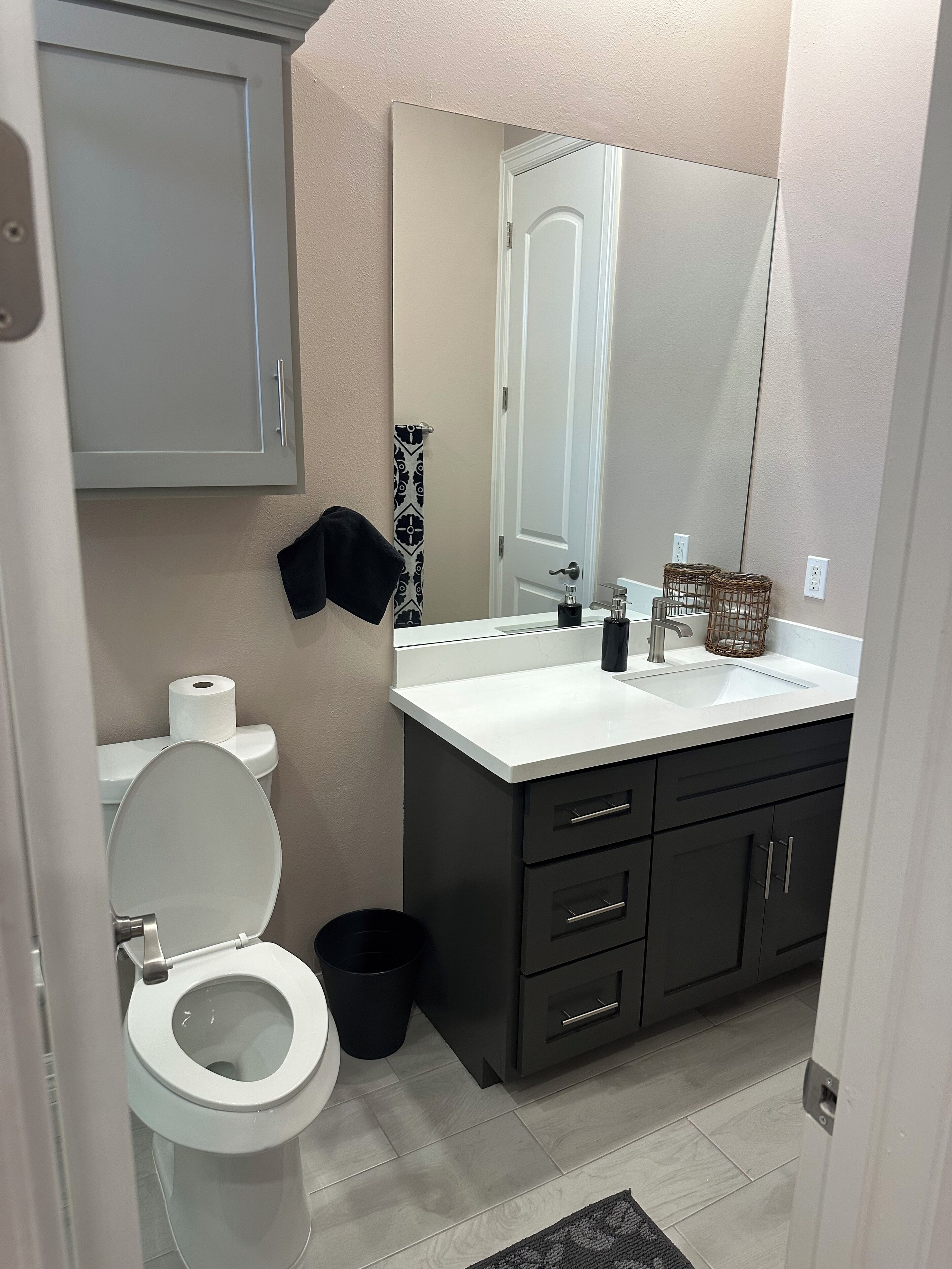Ein Badezimmer mit Toilette, Waschbecken, Spiegel und dunklen Schränken.