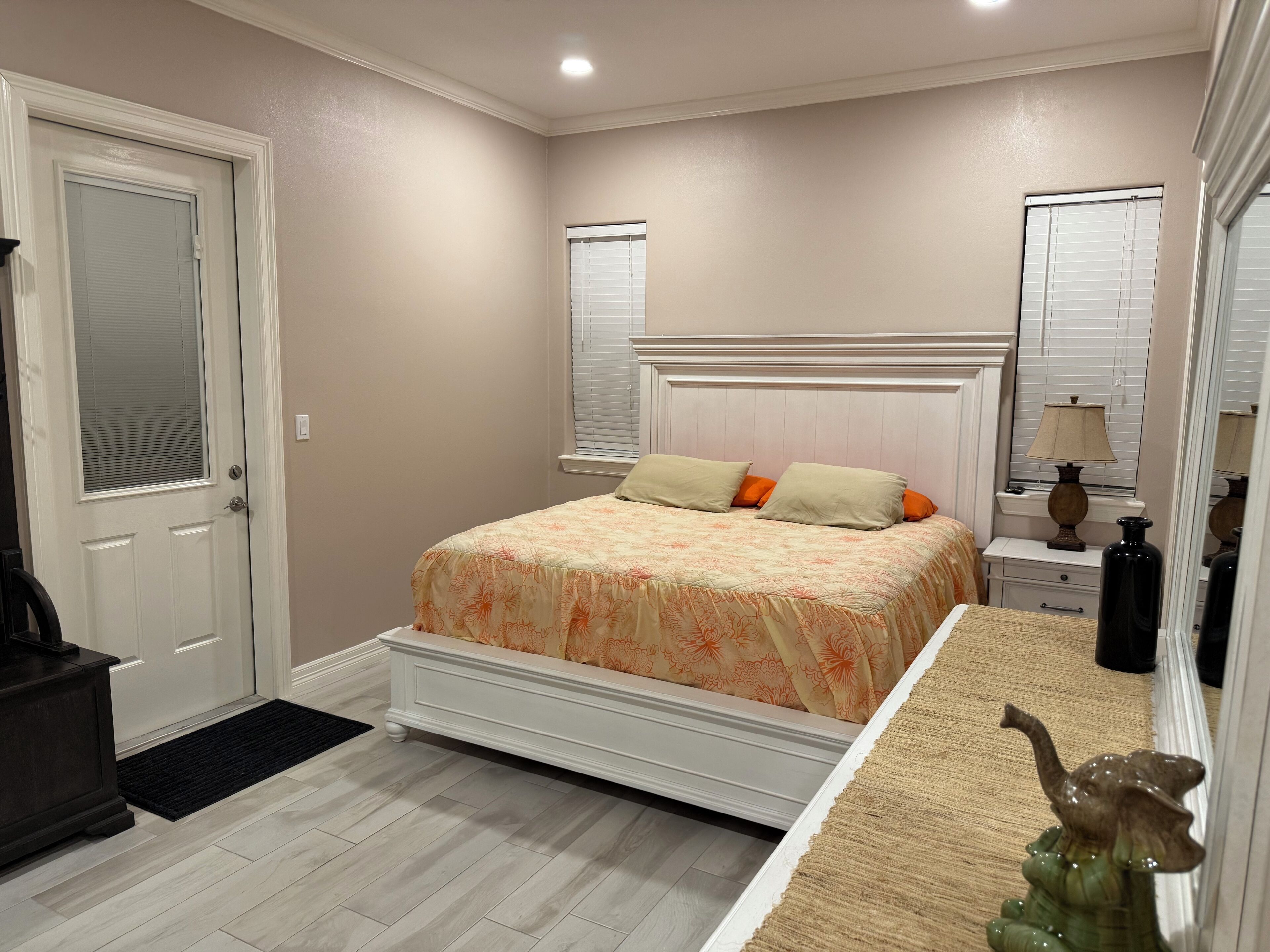 Une chambre à coucher comprenant un lit, des tables de chevet, une commode, un miroir et une porte.