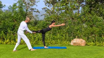 A person practicing yoga outdoors on a grassy area with trees and a rock in the background.