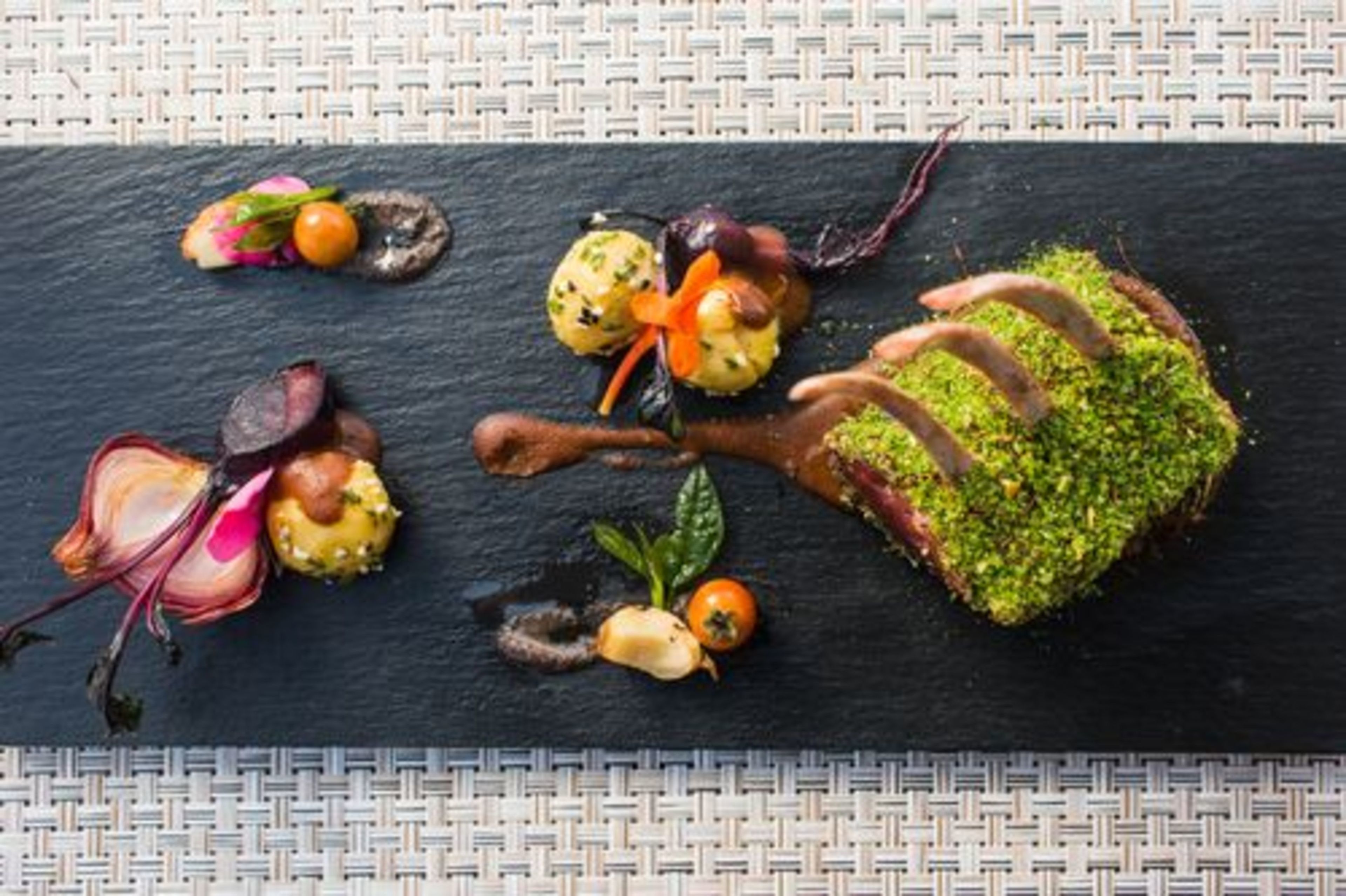 A black slate serving board with various food items, including a piece of meat, vegetables, and garnishes.