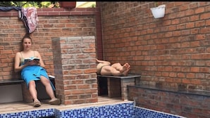 A swimming pool with blue mosaic tiles, a brick wall, and a person sitting on a bench reading a book. - Hue Four Seasons Hotel (Hue)