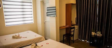 A hotel room with two beds, a desk, a chair, and a window with blinds.
