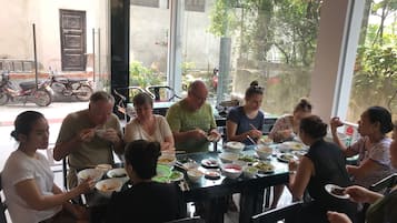 Un grupo de personas cenando en un restaurante al aire libre con amplias ventanas y vistas a la calle.