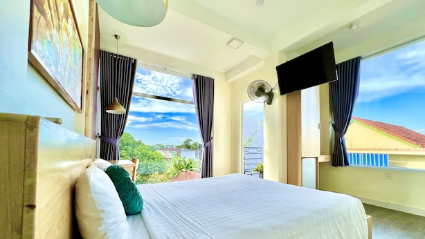 A bedroom with a bed, curtains, a TV, and a view of the outdoors. - Hue Four Seasons Hotel (Hue)