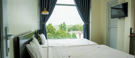 A hotel room with two beds, a TV, and a window with curtains.