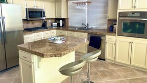 A modern kitchen with a granite countertop, stainless steel appliances, and a central island with bar stools.