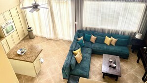 A living room with a sectional sofa, a coffee table, and a kitchen area with cabinets and a stove.