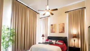 A bedroom with a bed, curtains, a ceiling fan, and a nightstand.