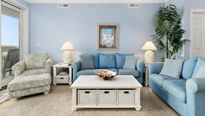 Un salon avec un canapé bleu, un fauteuil à motifs, une table basse blanche et une grande plante.