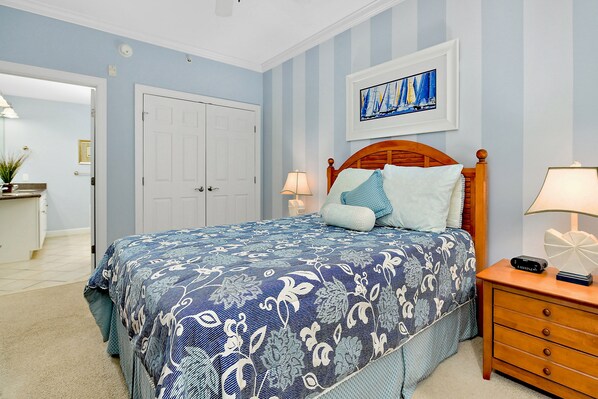 A bedroom with a bed, a nightstand, a dresser, a door, and a framed picture on the wall.