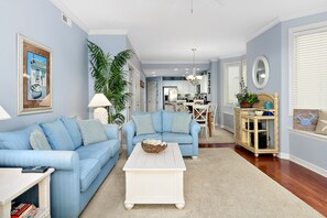 A living room with two blue sofas, a white coffee table, and a large potted plant.