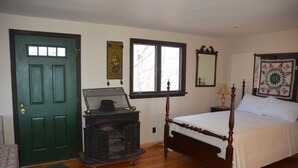 Un dormitorio con suelo de madera, una cama con dosel, una puerta verde, una ventana, un espejo y un edredón.