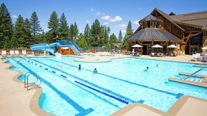 Ein großer Pool im Freien mit Wasserrutsche, Liegestühlen und einem Holzgebäude mit Außenbereich.