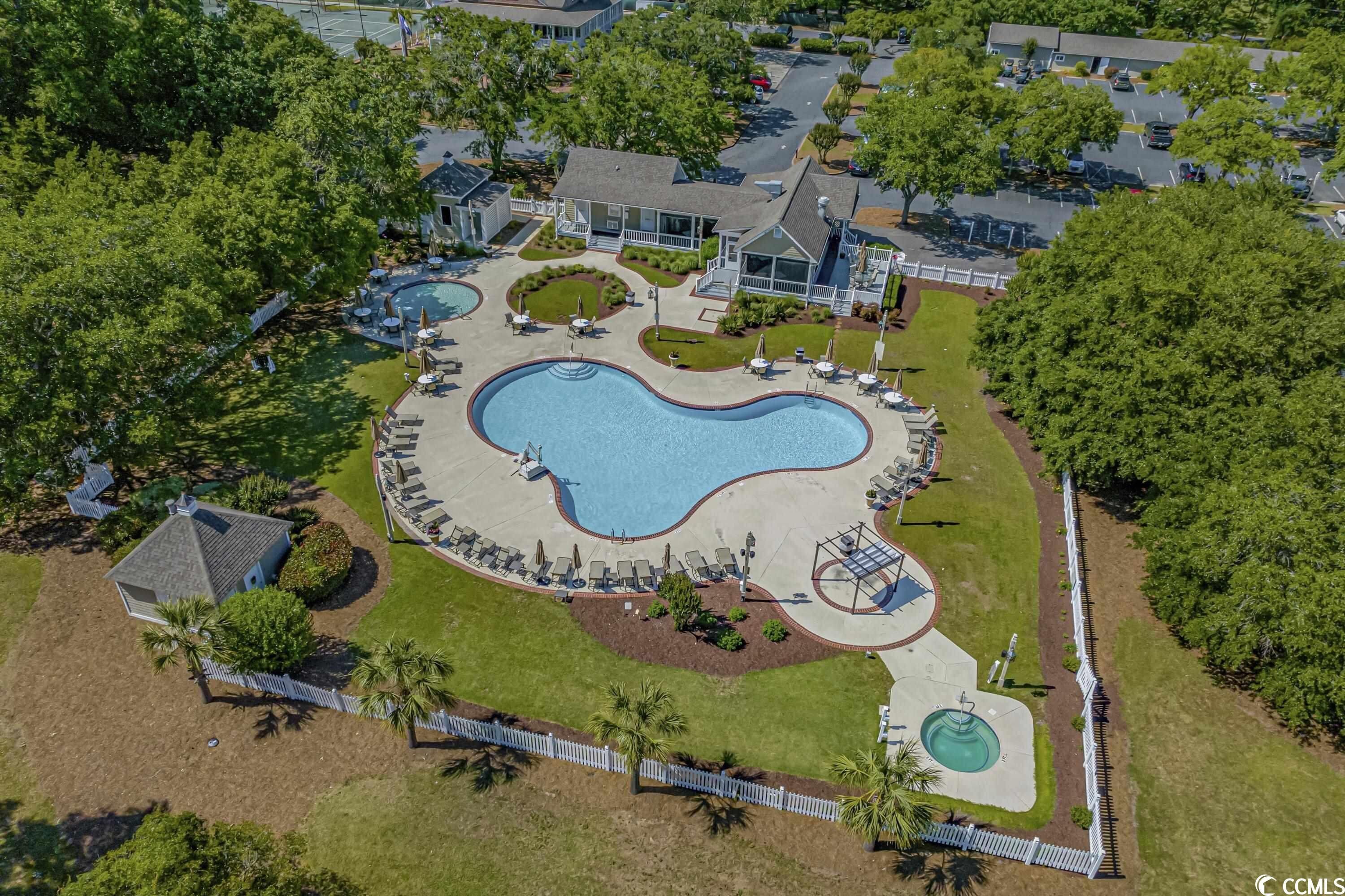Vue aérienne d’un quartier résidentiel avec une grande piscine, plusieurs maisons et des pelouses bien entretenues.