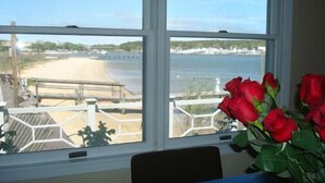 A room with a large window overlooking a beach and a wooden deck. - Hamptons Waterfront With Private Beach & Pool (Hampton Bays)