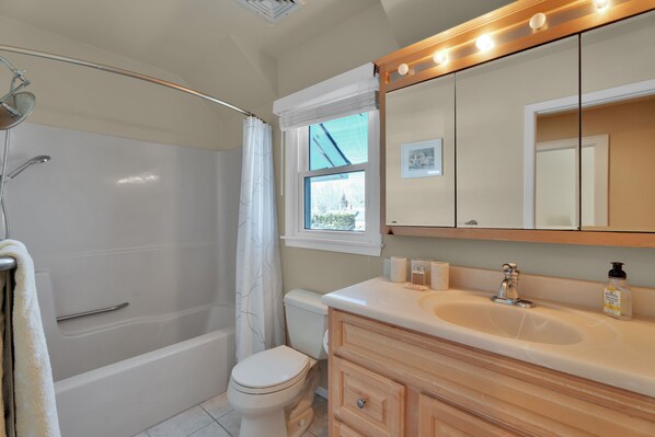 A bathroom with a bathtub, toilet, vanity with a mirror, and a window.