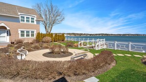 A house with a view of a lake, a white fence, and a swan statue in the yard. - Hamptons Waterfront With Private Beach & Pool (Hampton Bays)