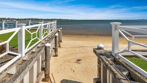 A wooden pier leading to a sandy beach with a clear view of the water and distant shoreline. - Hamptons Waterfront With Private Beach & Pool (Hampton Bays)