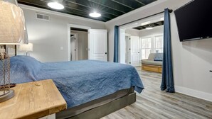 A bedroom with a bed, a wooden nightstand, a TV mounted on the wall, and a door leading to another room. - Lake Chillin’ at its finest! (Shelby County)
