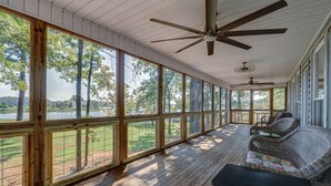 A covered porch with large windows overlooking a lake, wooden flooring, and wicker furniture. - Lake Chillin  ’ at its finest! (Shelby County)