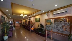 Un vestíbulo de hotel con mostrador de recepción, zona de estar y elementos decorativos como plantas y obras de arte.