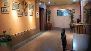 Un vestíbulo de hotel con cuadros enmarcados en las paredes, un mostrador de recepción y plantas en macetas.