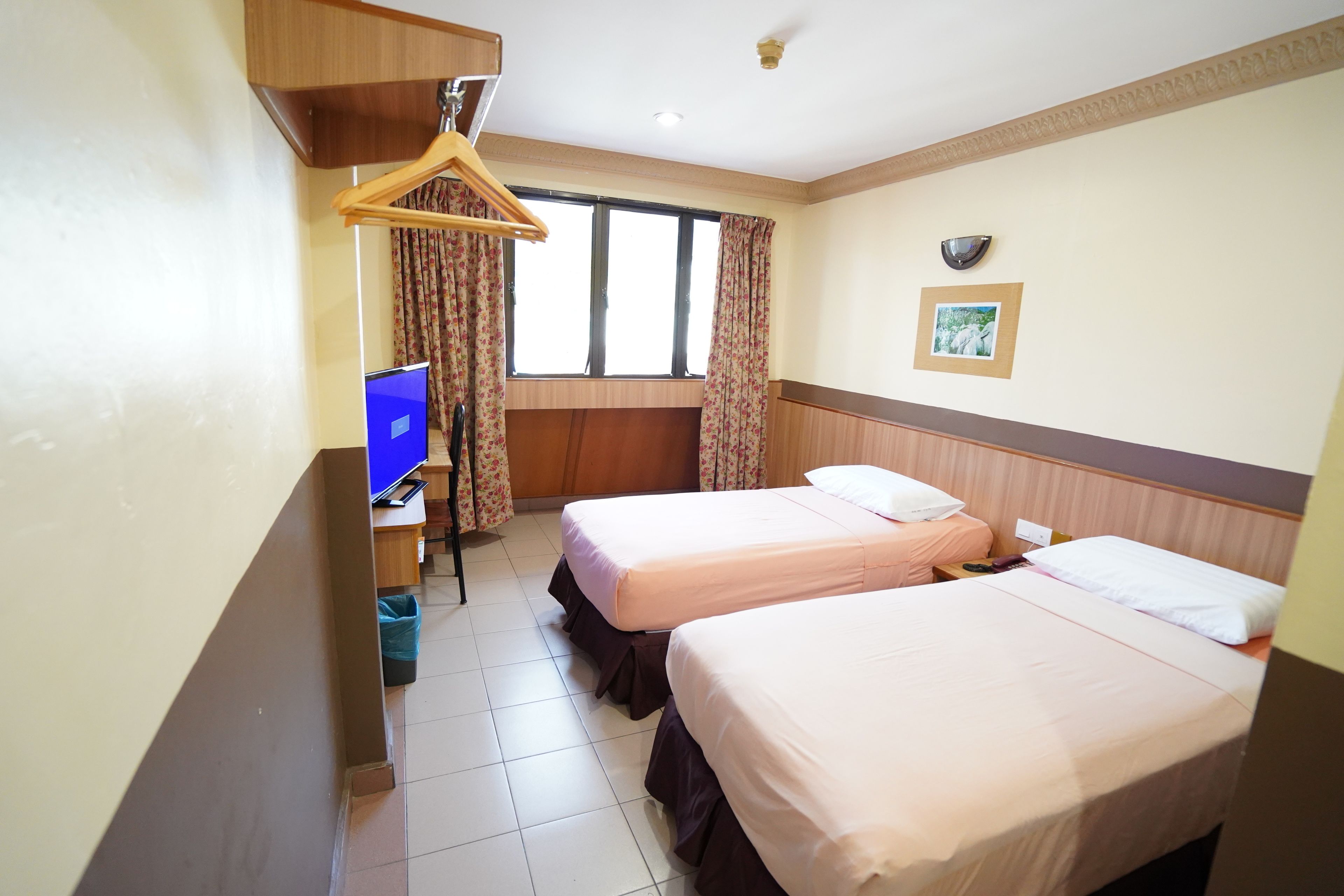 Une chambre d’hôtel avec deux lits, un bureau avec un ordinateur, une télévision et une fenêtre avec des rideaux.