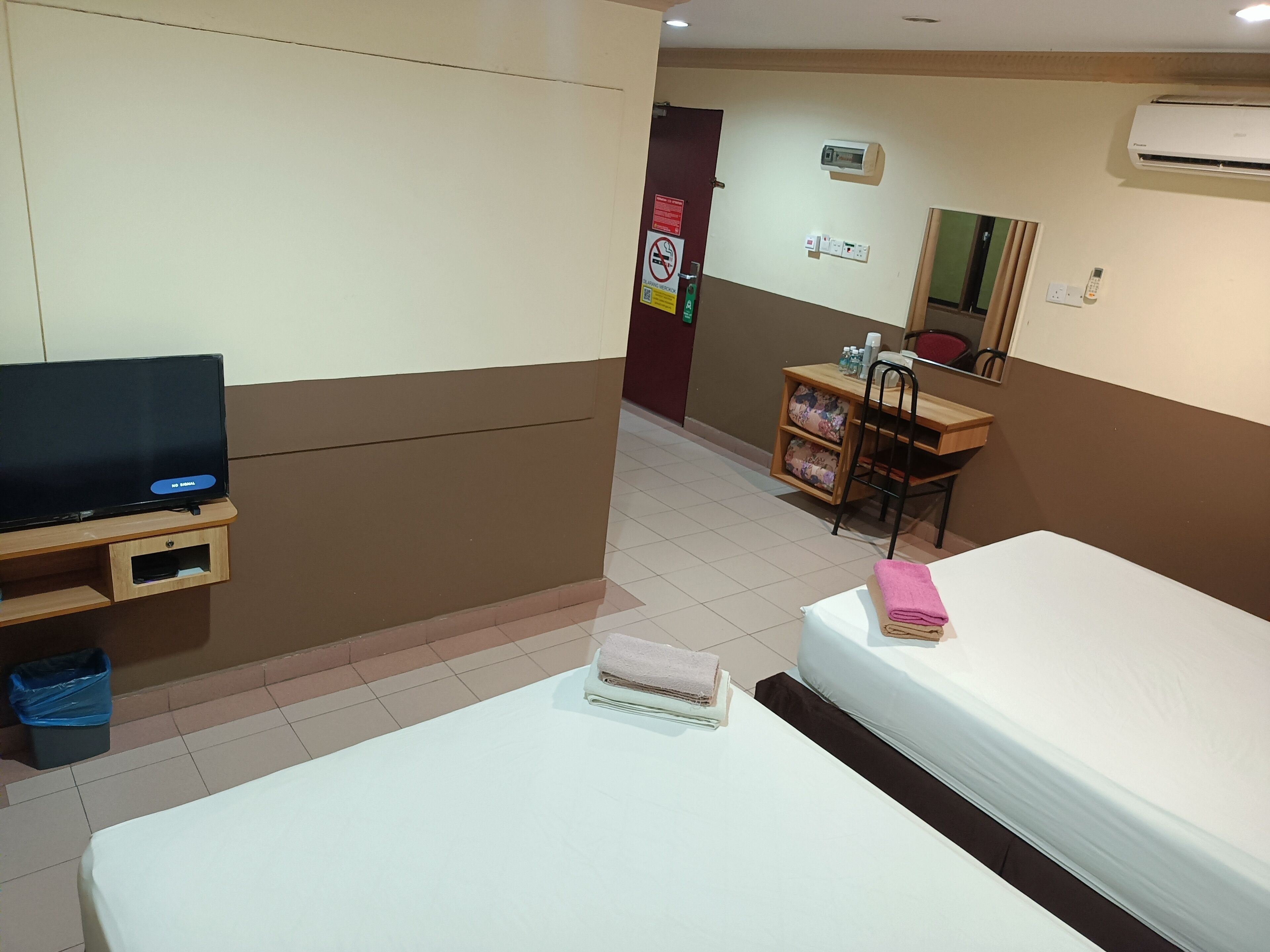A hotel room with a bed, a TV, a desk with a chair, and a small shelf with toiletries.