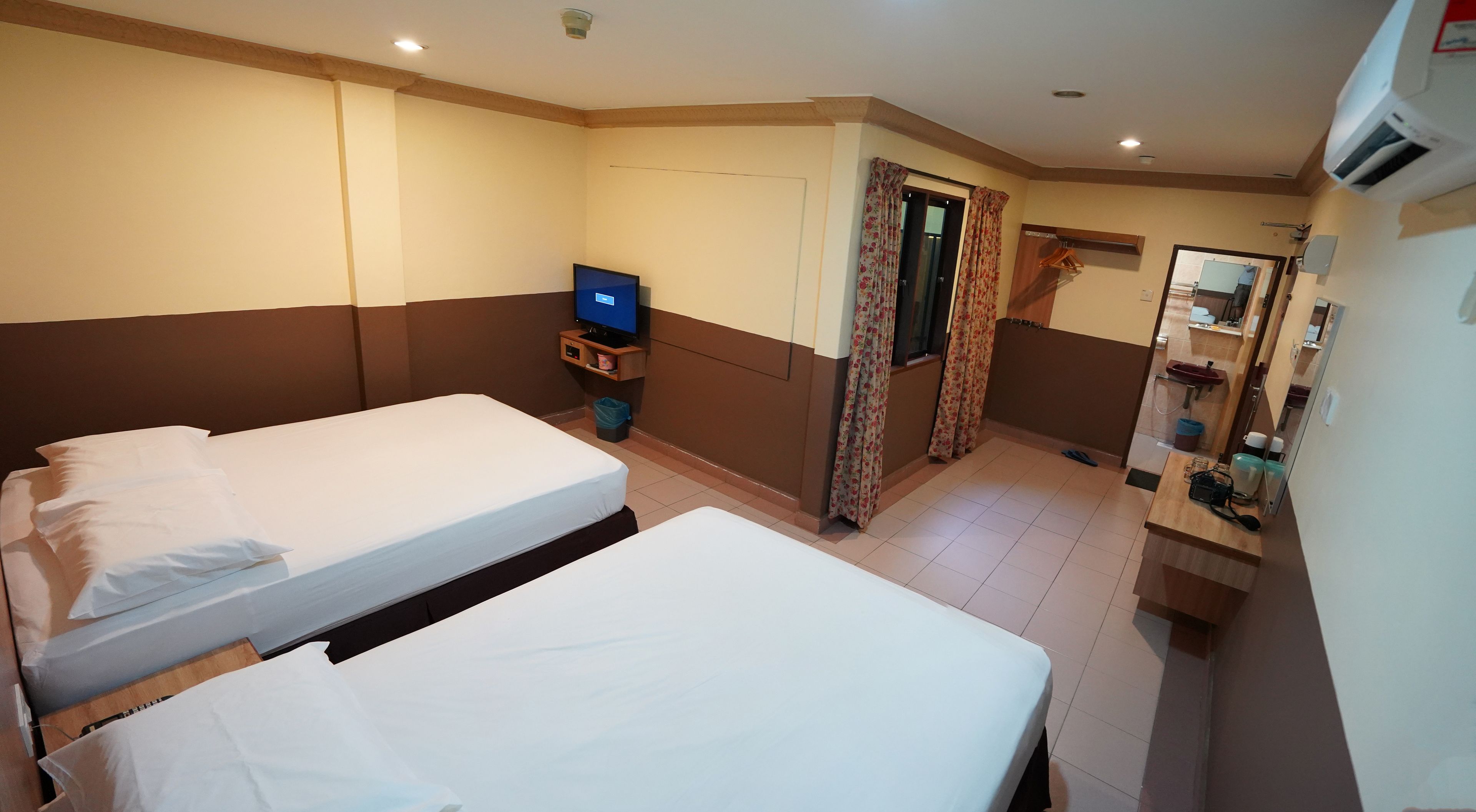 A hotel room with two beds, a television, a small table, a mirror, and a bathroom with a sink and toilet.