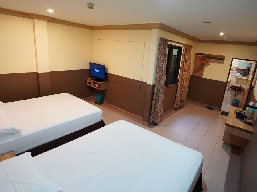 A hotel room with two beds, a television, a small table, a mirror, and a bathroom with a sink and toilet.