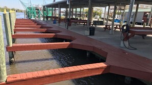 A wooden dock extending into a body of water with a covered seating area and picnic tables in the background.