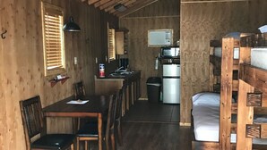 A rustic cabin interior with a dining area, kitchen, and bunk beds.