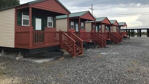 A row of small, single-story cabins with red railings and green trim, situated on a gravel surface.