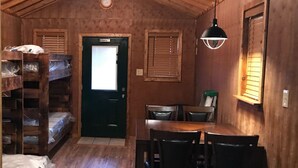 A cabin with a wooden interior, a dining area with a table and chairs, bunk beds, a door with a window, and a ceiling fan.