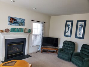 A living room with a fireplace, a television, and two green armchairs.