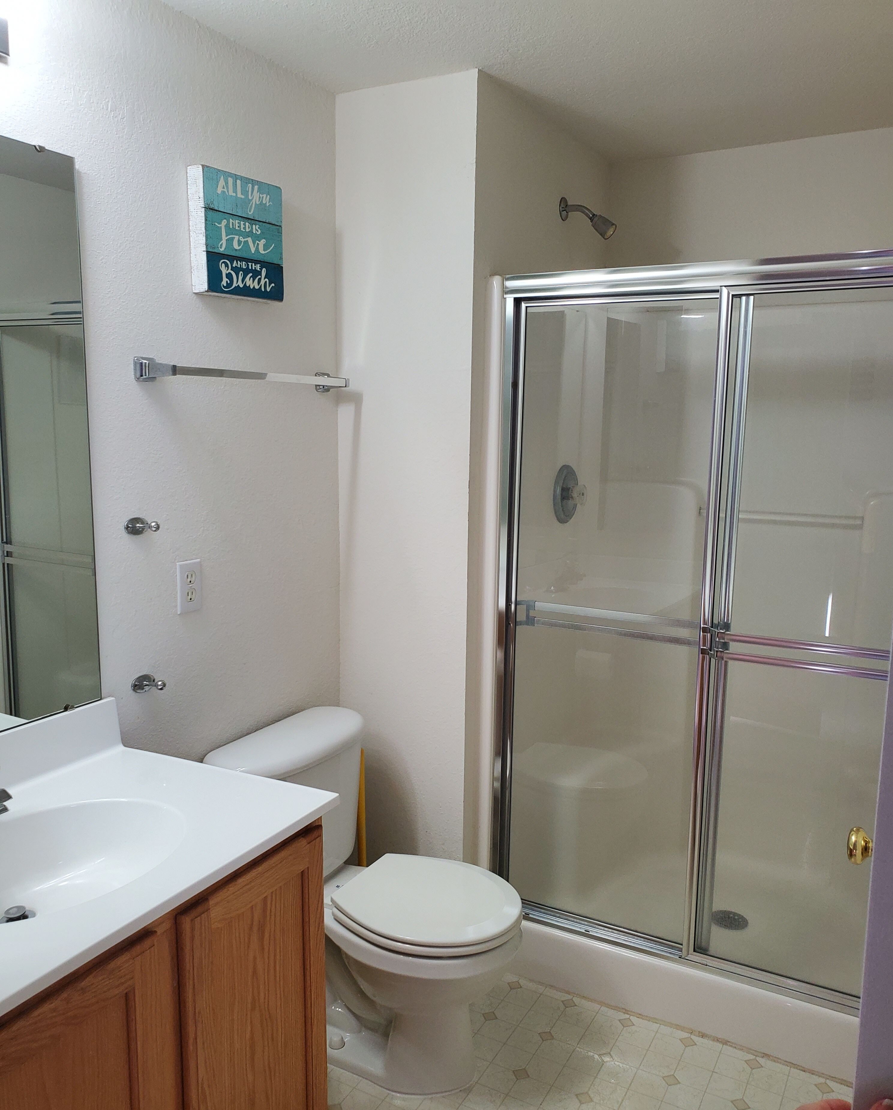 Une salle de bain avec une douche à parois de verre, des toilettes blanches et un meuble-lavabo en bois avec un évier.