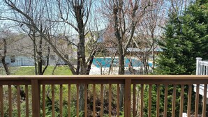 Une terrasse en bois offrant une vue sur un jardin avec une piscine, des arbres et une maison en arrière-plan.