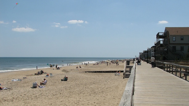 Une plage avec une promenade en bois, des vacanciers et un ciel dégagé.