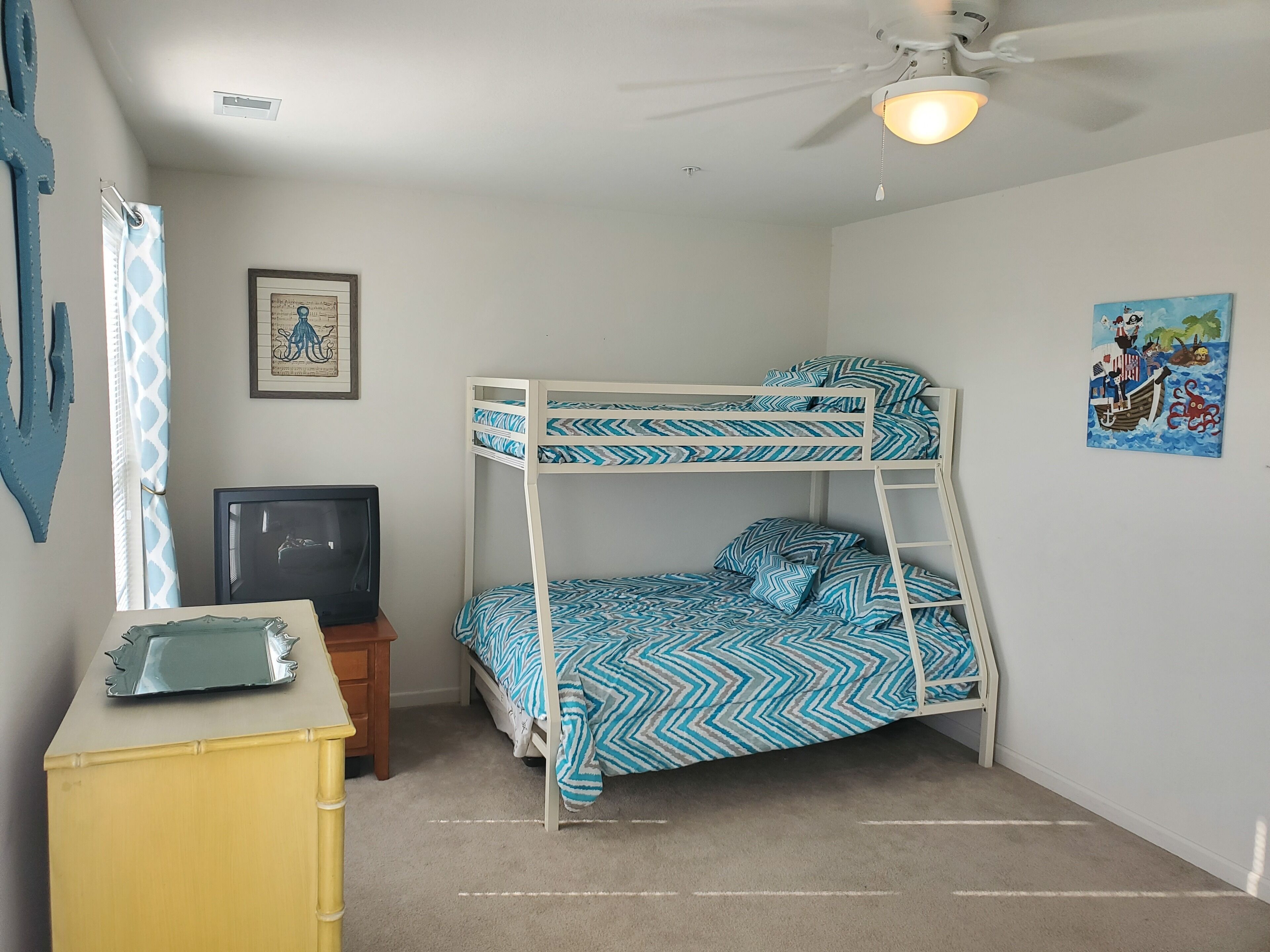 A bunk bed room with a ceiling fan, a small desk with a television, and a framed picture on the wall.